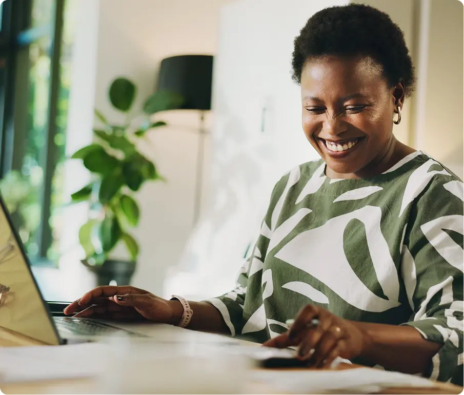 A Black woman sitting at a table, researching Invoice Discounting on her laptop and smiling.