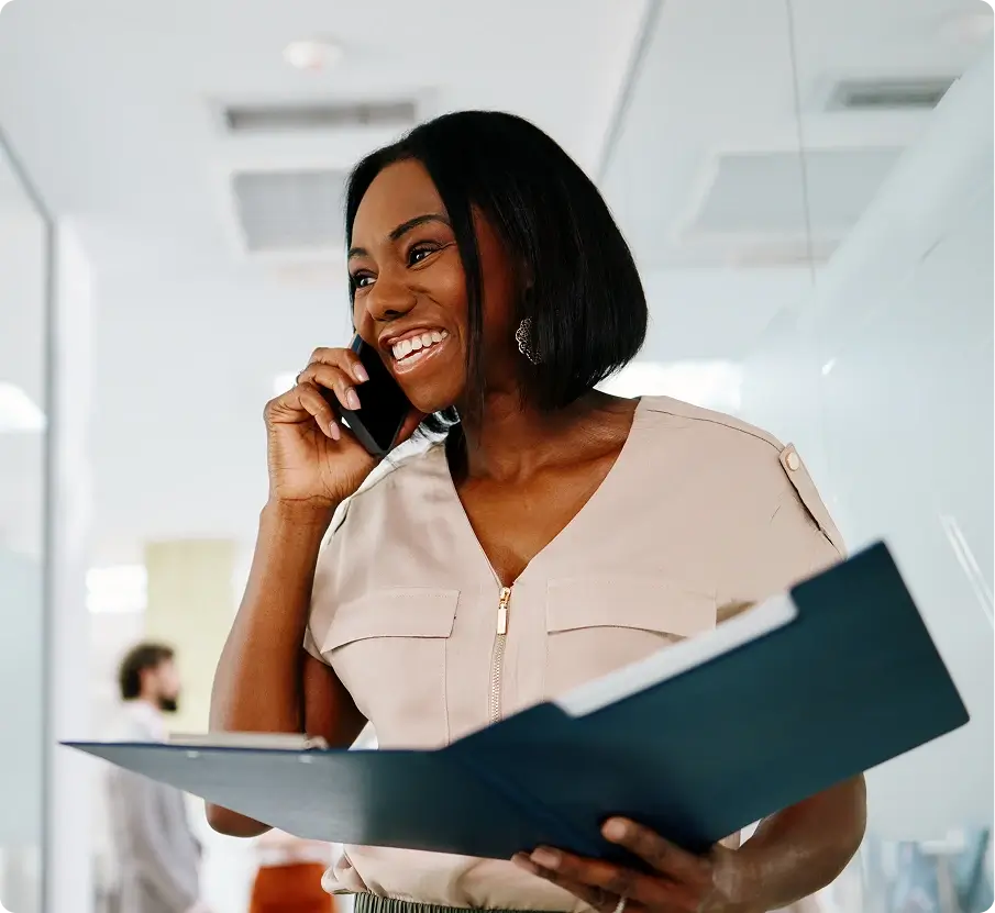 A Black woman smiling on a call, holding a folder.